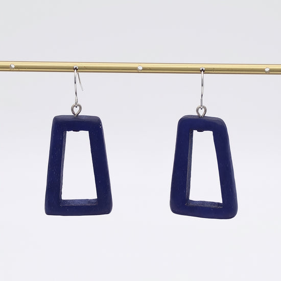 Navy blue square earrings hanging from a gold rod against a white background