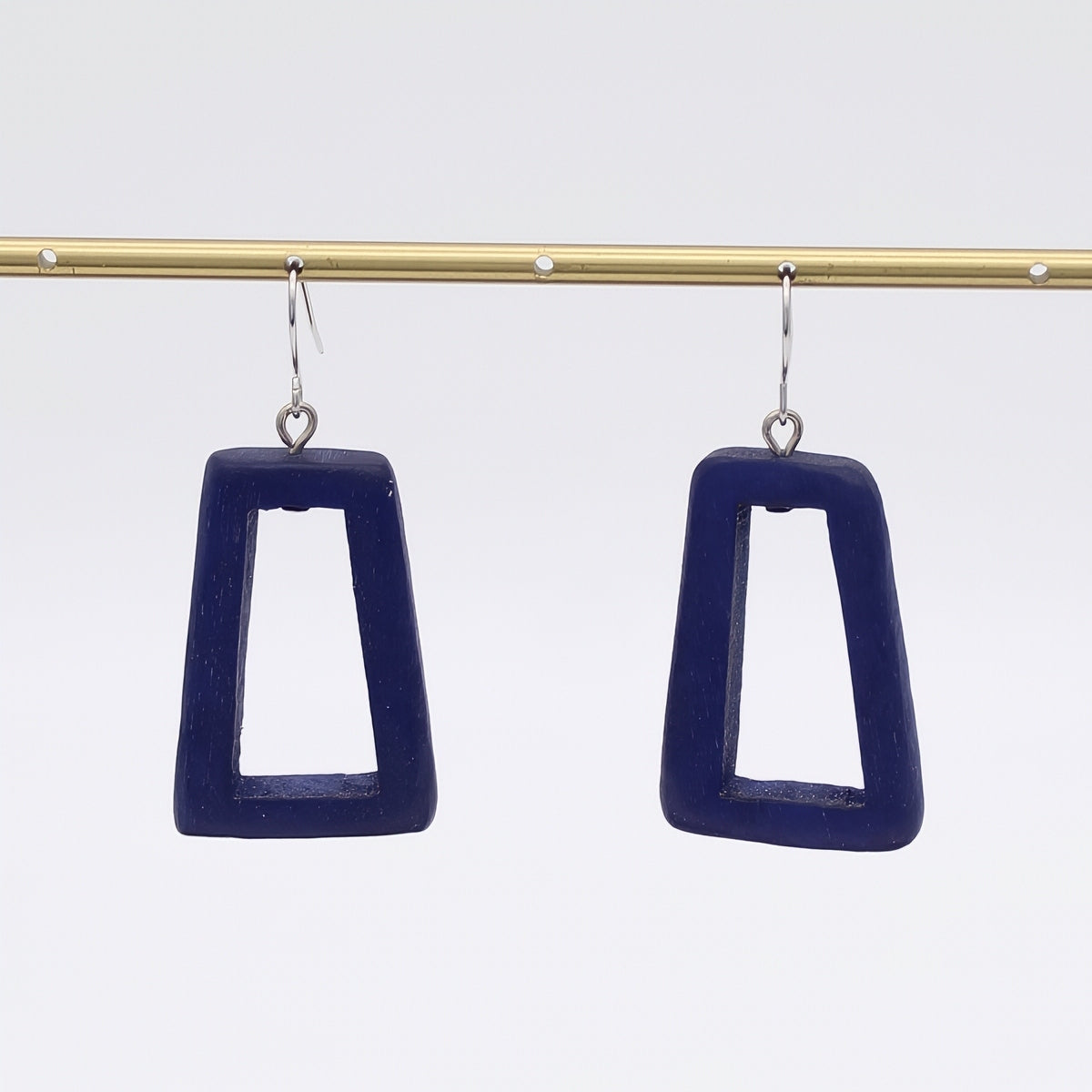 Navy blue square earrings hanging from a gold rod against a white background