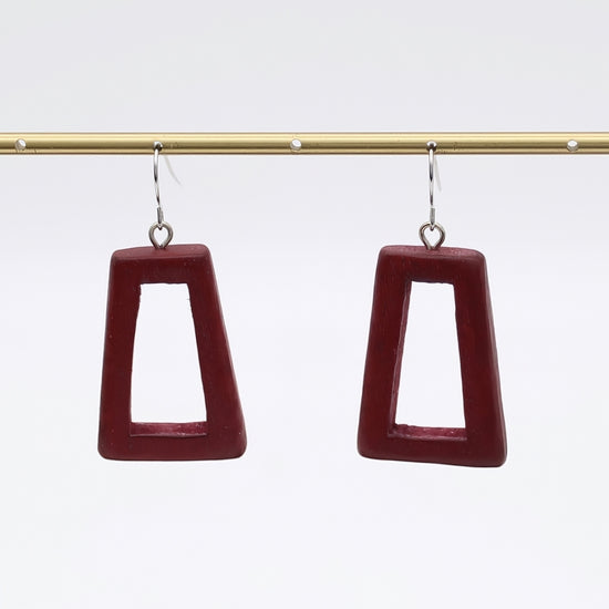 Pair of maroon square earrings on a gold rod against a white background