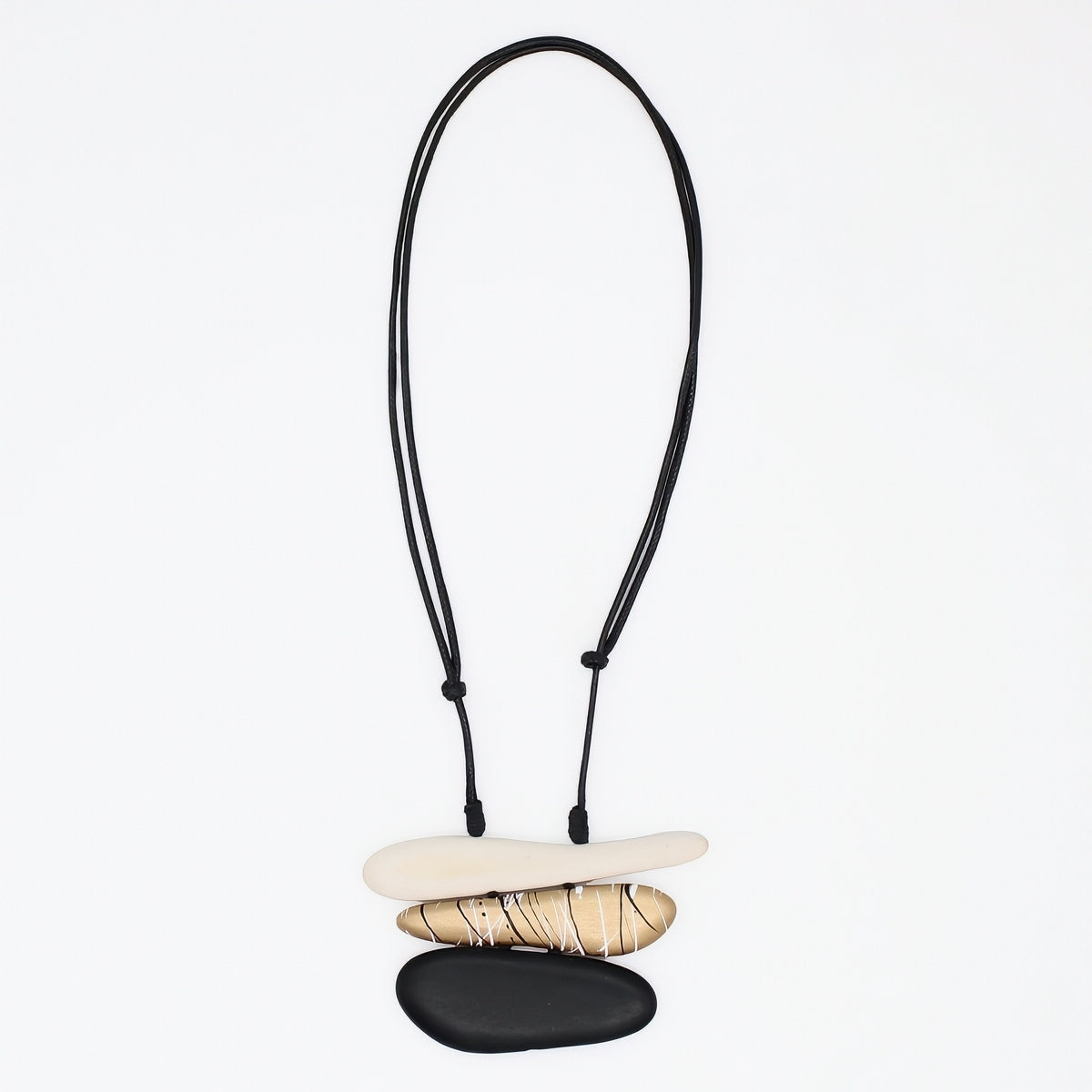 A minimalist necklace featuring three stacked natural stones in cream, tan, and black, suspended on a black adjustable cord against a plain white background.