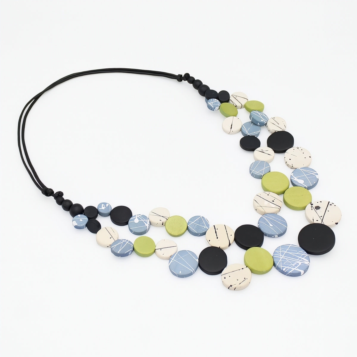 A multi-strand statement necklace featuring round, textured ceramic beads in black, light blue, olive green, and cream, suspended on a black cord, shown against a plain white background.
