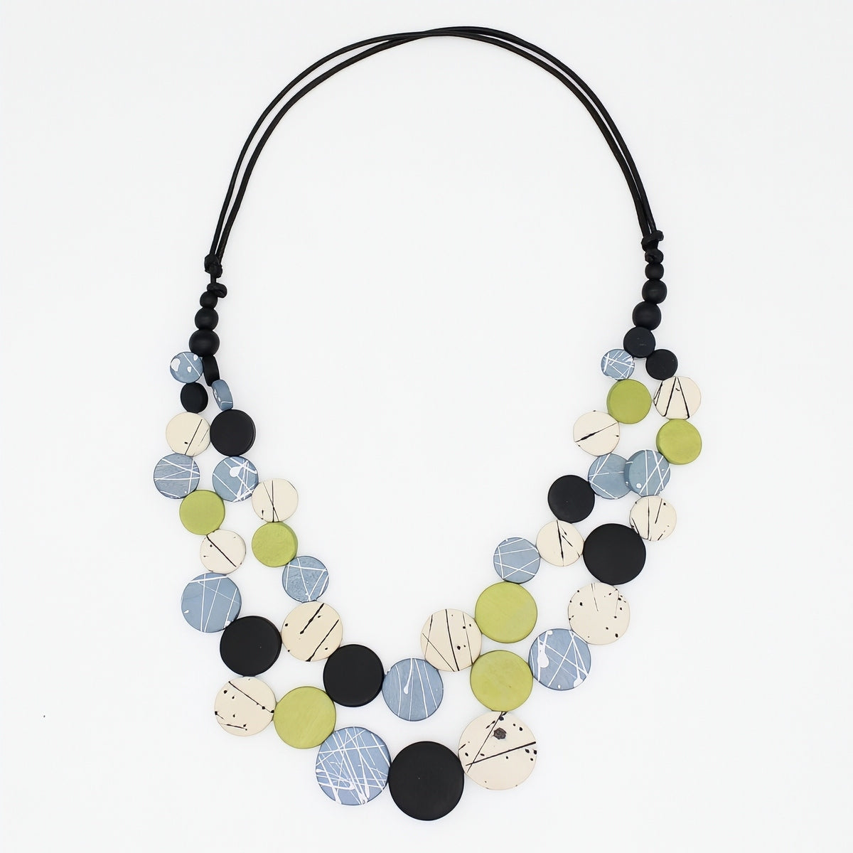 A multi-strand statement necklace featuring circular wooden discs in black, light blue, olive green, and cream with abstract line patterns, suspended on a black cord against a white background.