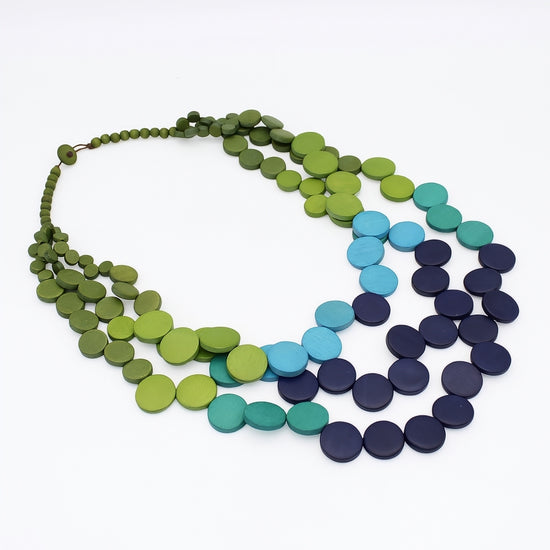 A multi-strand disc necklace made of flat circular beads in shades of olive green, lime green, turquoise, teal, and dark navy blue, arranged on a plain white background.