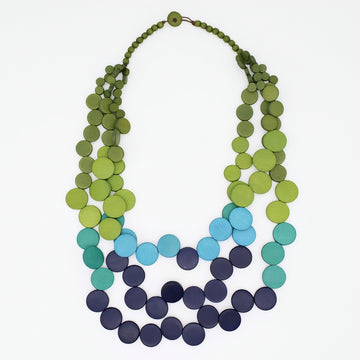 A multi-strand beaded necklace made of flat circular discs, featuring a color gradient from olive and lime green at the top, through light blue, teal, and dark navy at the bottom, displayed on a clean white background.