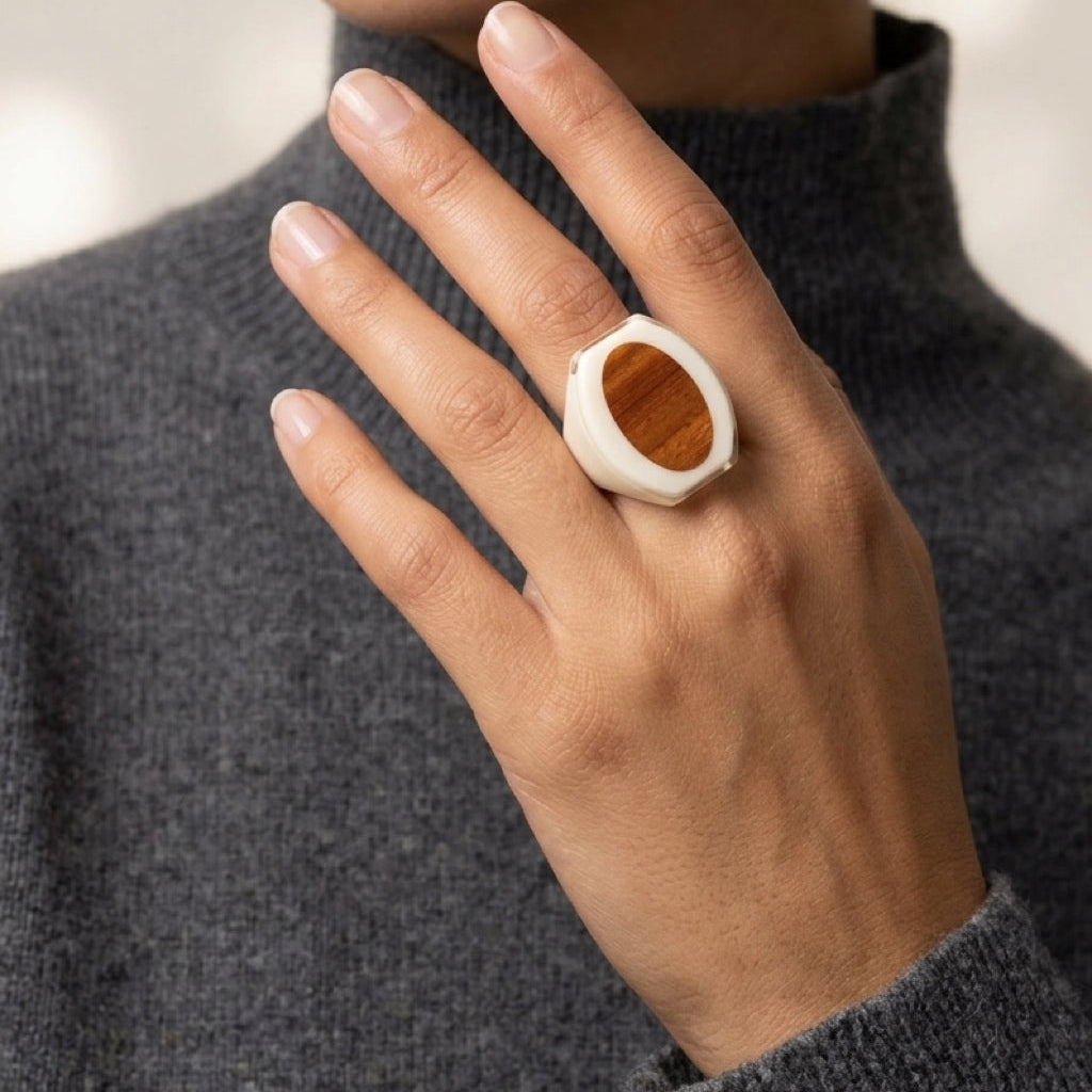 Close-up of a hand wearing a ring with a wooden center, against a neutral background.