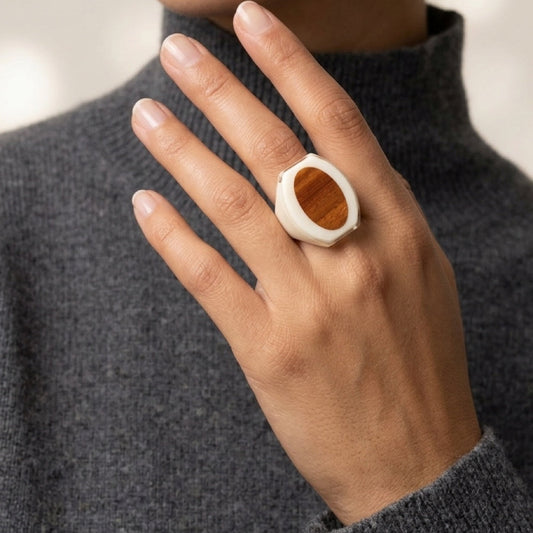 Close-up of a hand wearing a ring with a wooden center, against a neutral background.