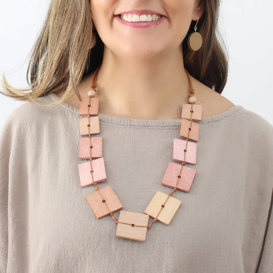 Woman wearing a long, pink square pendant necklace against a neutral background