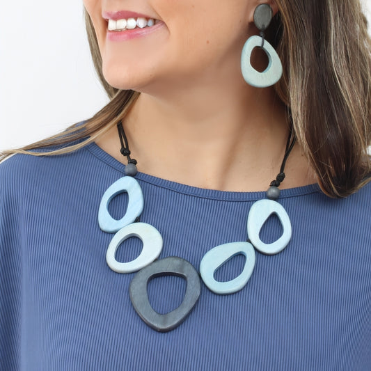 Woman wearing a necklace and earrings with large, colorful, abstract pendants.