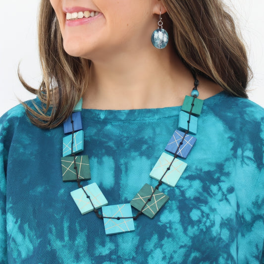 Woman wearing a blue and green geometric necklace and earrings on a white background