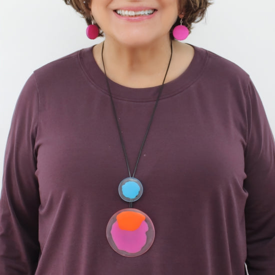 Person wearing a purple shirt with a colorful necklace against a white background
