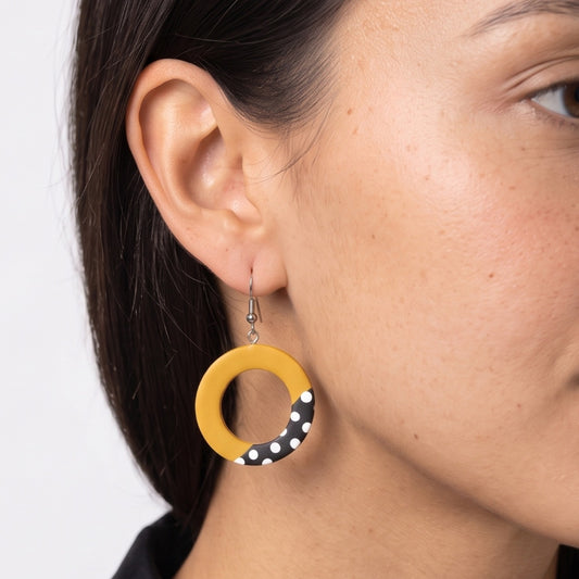 A close-up of a woman's ear wearing a yellow circular drop earring with a black and white polka dot section at the bottom.