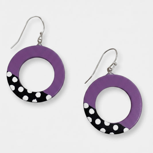A pair of RESIN hoop earrings with a purple top half and a black bottom half decorated with white polka dots, hanging from silver fishhook wires on a light gray background.
