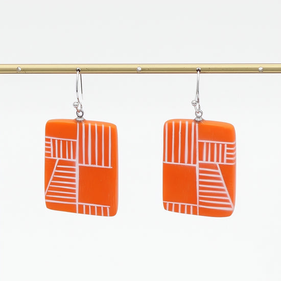 Orange earrings with white geometric pattern on a white background