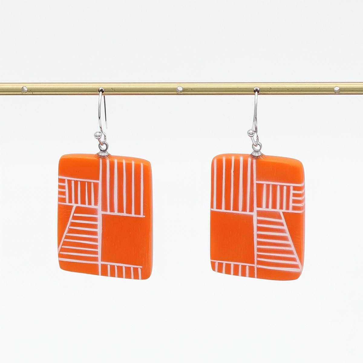 Orange earrings with white geometric pattern on a white background
