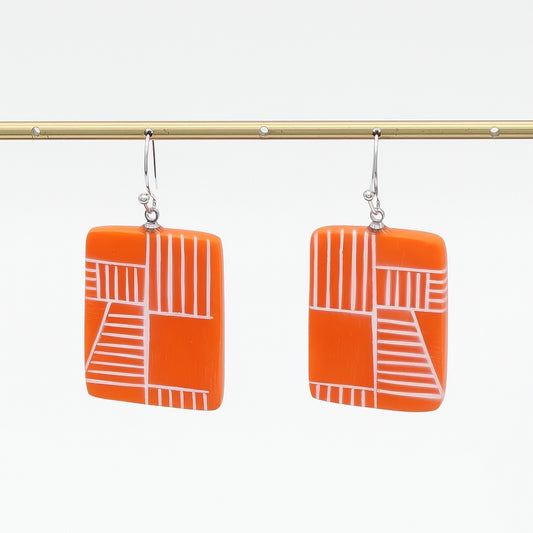 Orange earrings with white geometric pattern on a white background