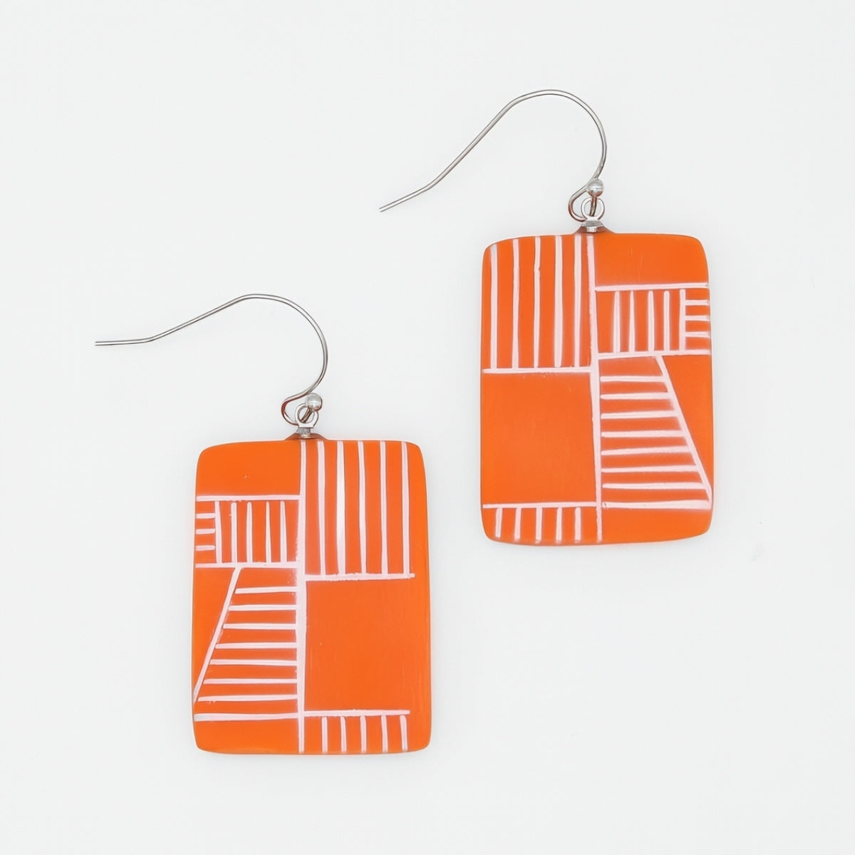 Orange earrings with white geometric patterns on a light gray background
