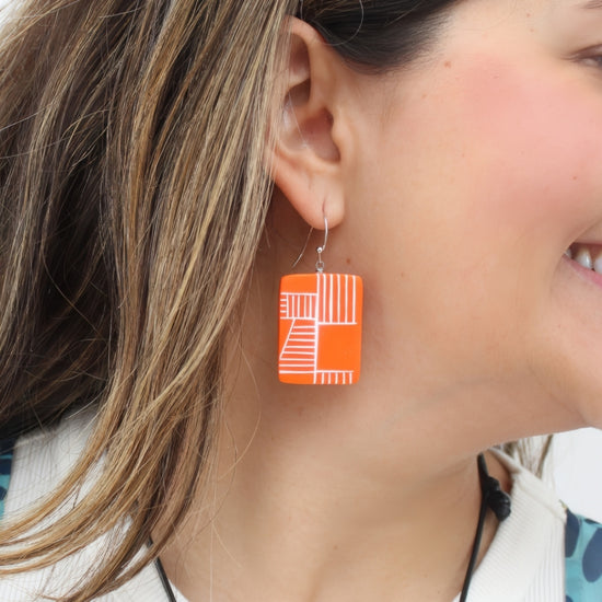 Close-up of a woman wearing orange geometric earrings.