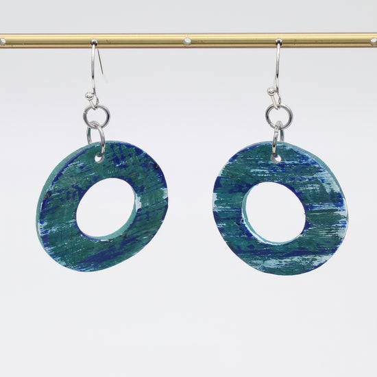 Blue and green circular earrings hanging from a gold rod against a white background
