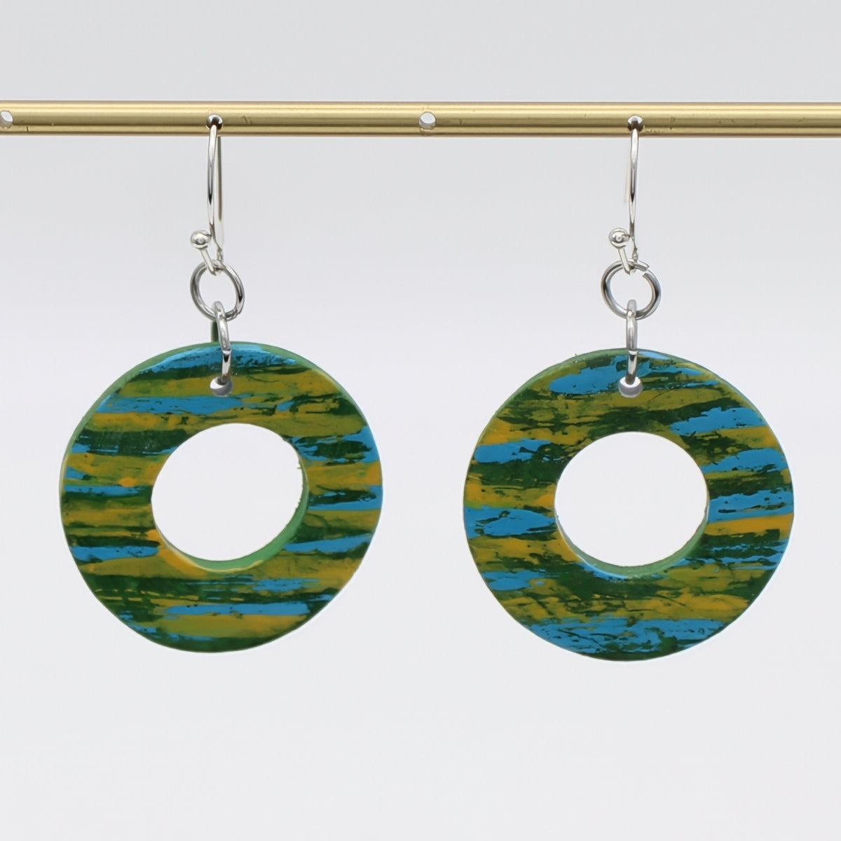 Pair of earrings with circular design in green and blue on a white background