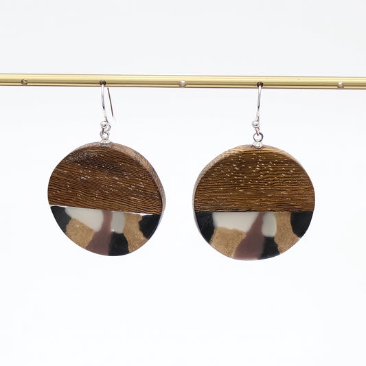A pair of round drop earrings hanging from silver hooks, featuring a split design with a textured brown wood top half and a marbled resin bottom half in brown, black, cream, and beige.