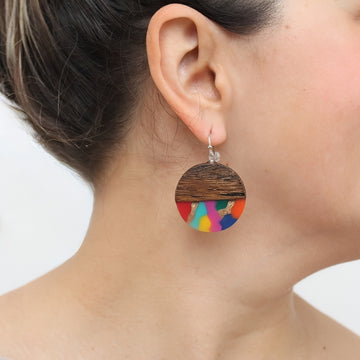 Close-up of a person wearing colorful wooden earrings with a white background