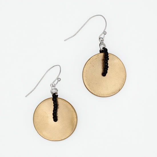 A pair of dangle earrings featuring textured, hammered circular gold-toned discs suspended from silver fishhook wires with a small black beaded accent, shown on a plain white background.