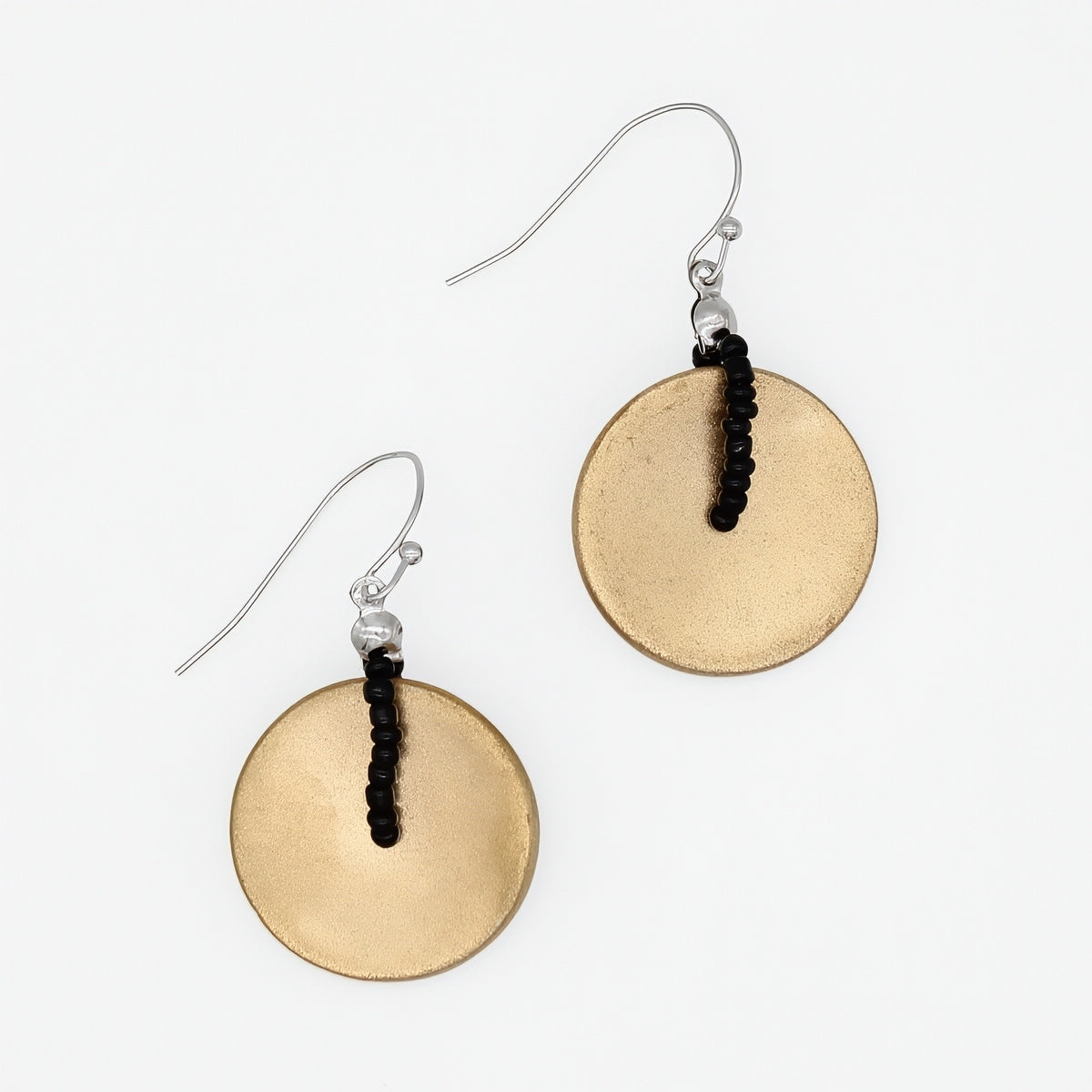 A pair of dangle earrings featuring textured, hammered circular gold-toned discs suspended from silver fishhook wires with a small black beaded accent, shown on a plain white background.