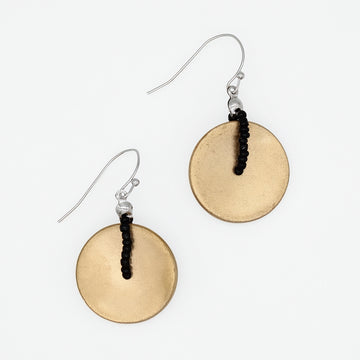A pair of dangle earrings featuring textured, hammered circular gold-toned discs suspended from silver fishhook wires with a small black beaded accent, shown on a plain white background.