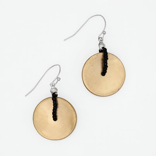A pair of dangle earrings featuring textured, hammered circular gold-toned discs suspended from silver fishhook wires with a small black beaded accent, shown on a plain white background.