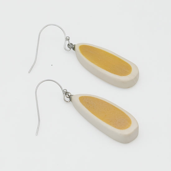 Pair of earrings with yellow and beige oval-shaped pendants on a white background