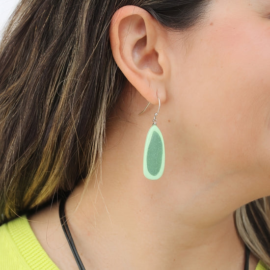 Green teardrop earring worn by a person with dark hair.