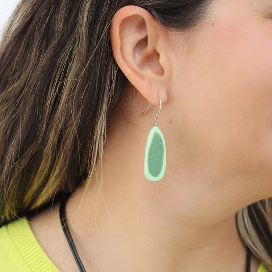 Green teardrop earring worn by a person with dark hair.