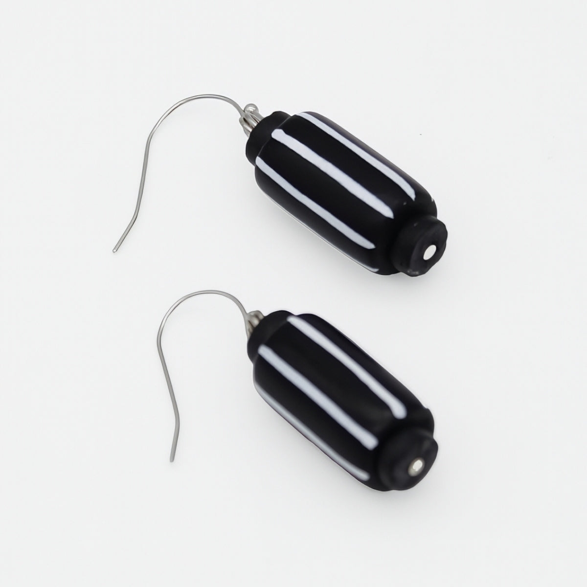 A pair of drop earrings featuring glossy black cylindrical beads with three horizontal white stripes, suspended from silver fishhook wires on a plain white background.