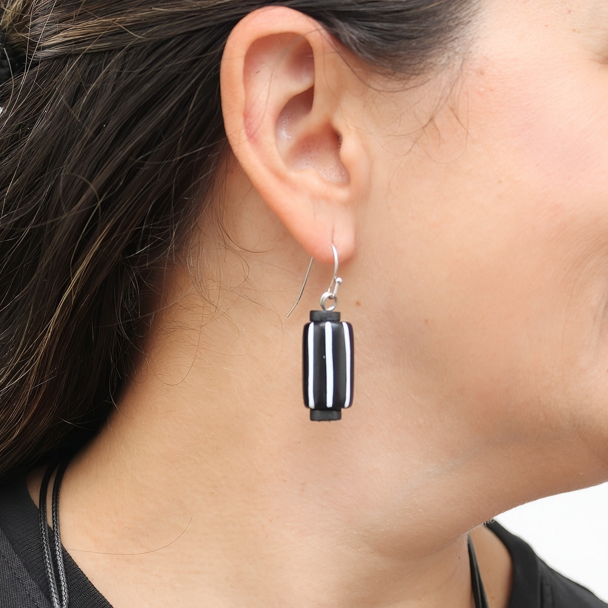 A close-up of a person's ear wearing a single drop earring with a black and white striped rectangular charm on a silver hook.