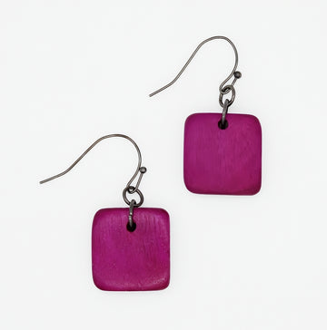 A pair of square-shaped drop earrings with a textured magenta-purple wooden disc and a dark metal fishhook ear wire, shown on a plain white background.