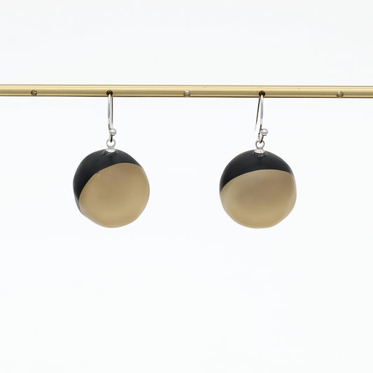 A pair of modern dangle earrings with a split black and golf design, hanging from silver hooks on a gold horizontal bar against a white background.