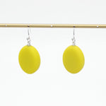 A pair of bright yellow oval drop earrings with silver fishhook wires, hanging from a gold-colored horizontal display bar against a plain white background.