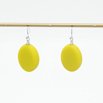 A pair of bright yellow oval drop earrings with silver fishhook wires, hanging from a gold-colored horizontal display bar against a plain white background.