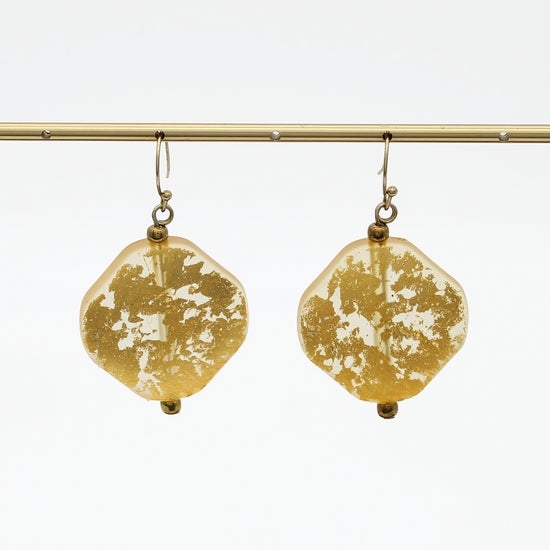 Pair of gold resin drop earrings hanging from display bar