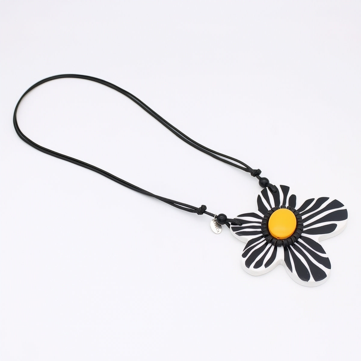 Black and white flower-shaped pendant with a yellow center on a black cord against a white background