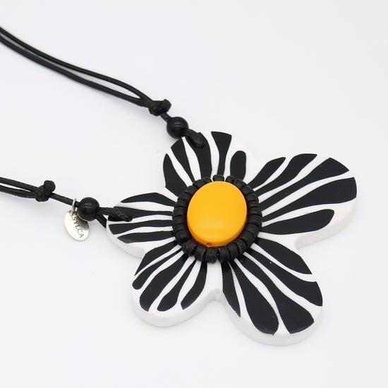 Black and white flower-shaped pendant with a yellow center on a black cord against a white background