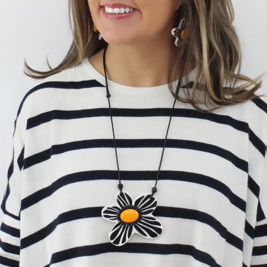 Woman wearing a black and white striped shirt with a necklace featuring a large flower pendant.