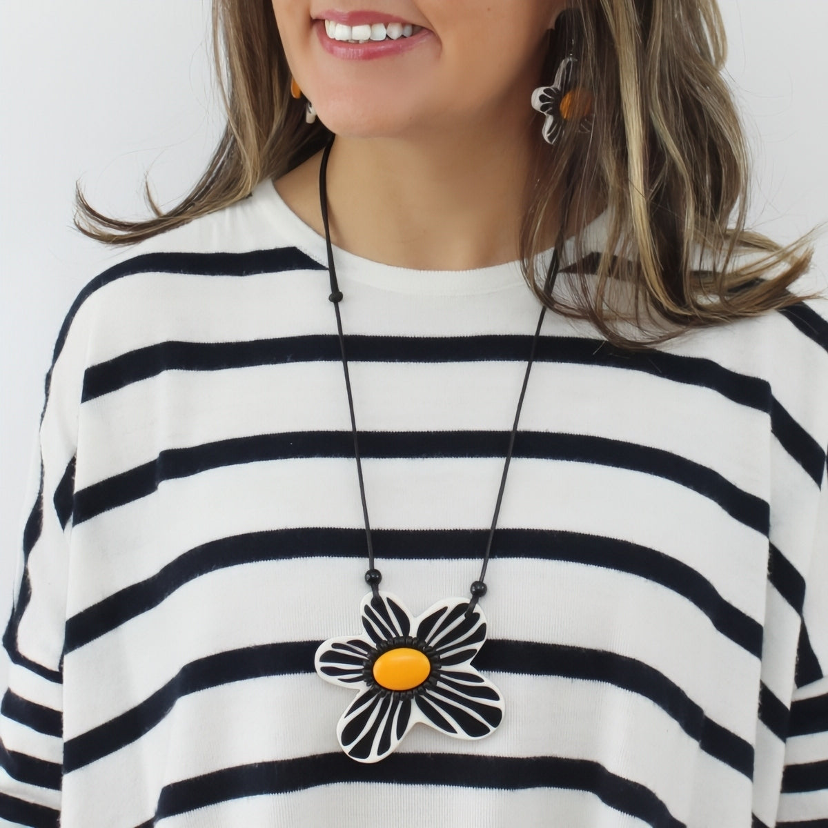 Woman wearing a black and white striped shirt with a necklace featuring a large flower pendant.