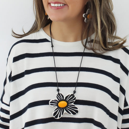 Woman wearing a black and white striped shirt with a necklace featuring a large flower pendant.