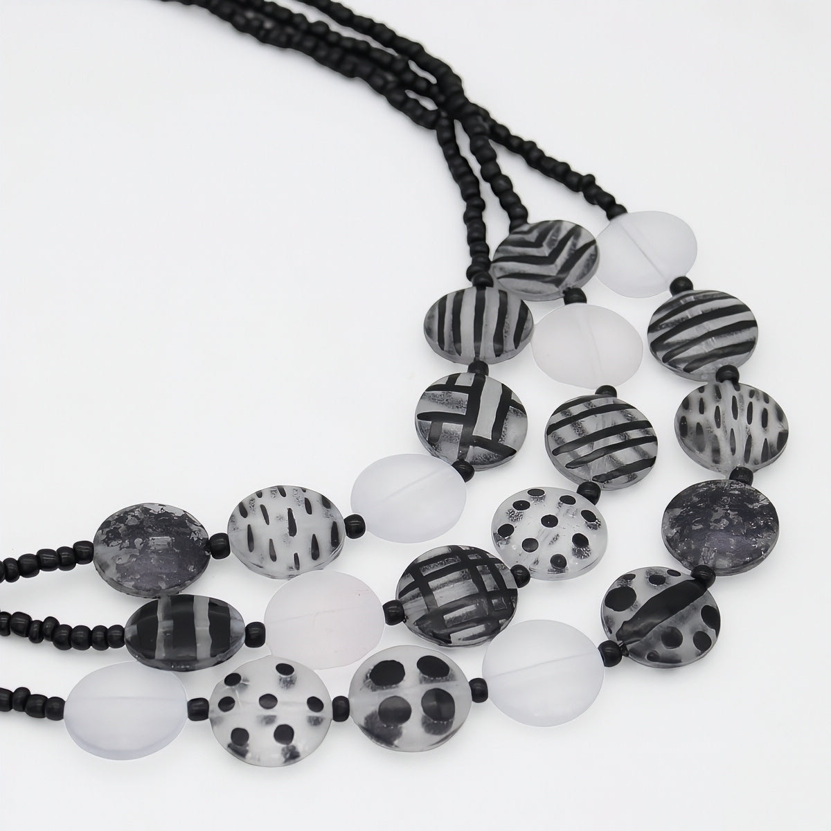 A multi-strand beaded necklace featuring black and white patterned round beads, translucent white beads, and black cord, displayed on a clean white background.