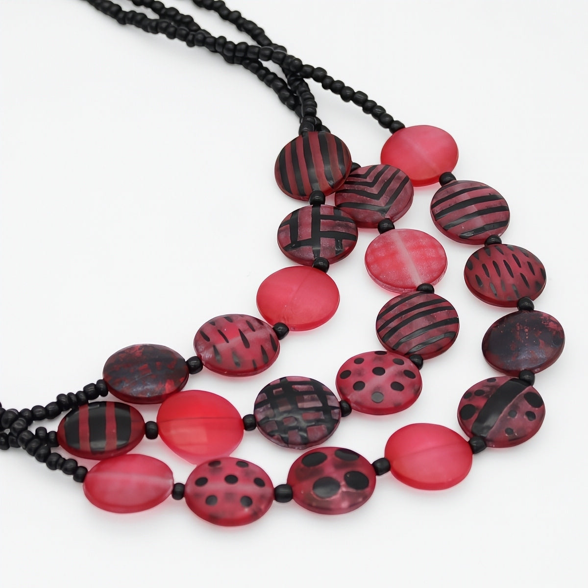 A multi-strand statement necklace featuring red and black patterned oval beads on a white background.