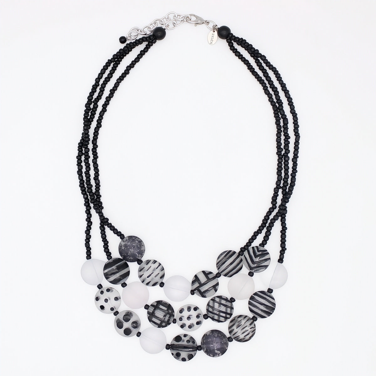 A multi-strand statement necklace featuring black beaded cords and a tiered arrangement of round beads in black, white, and gray patterns, including stripes, polka dots, and marbled textures, on a plain white background.