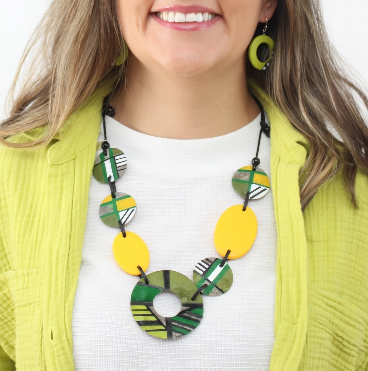 Woman wearing a colorful necklace with a white shirt and green jacket.