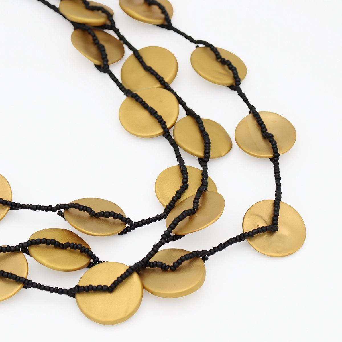 A multi-strand statement necklace featuring flat, brushed gold oval disc charms threaded on a black beaded cord, displayed on a clean white background.