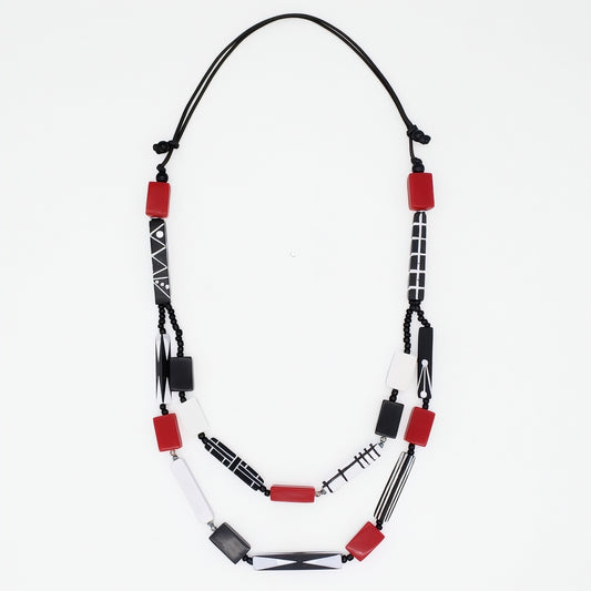 A beaded necklace with red rectangular beads, white beads, and black patterned beads on a black cord, displayed against a plain white background.